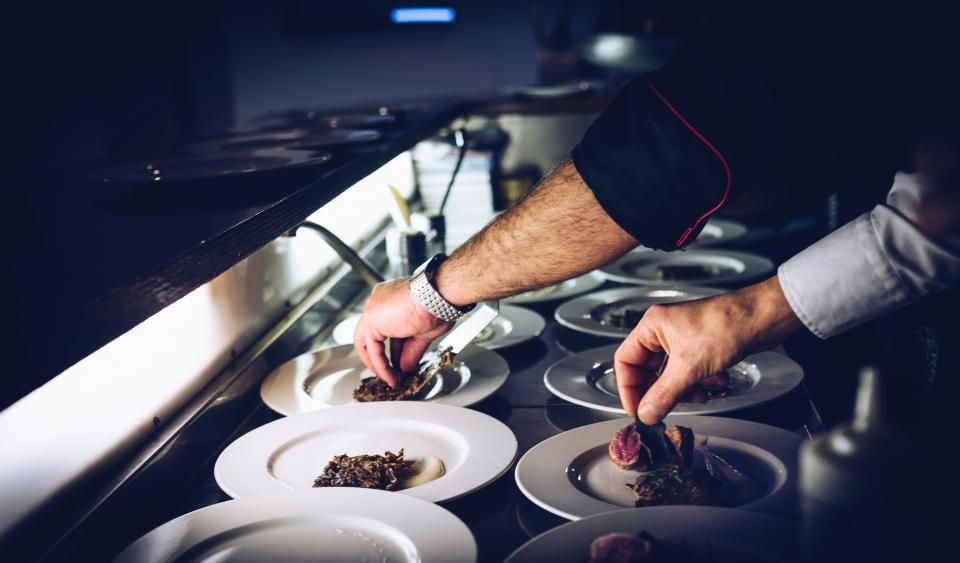 Les mains d'un cuisinier dressant des assiettes à la pince